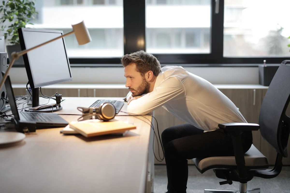 Office worker slumped forward at a desk with the head craned toward a monitor